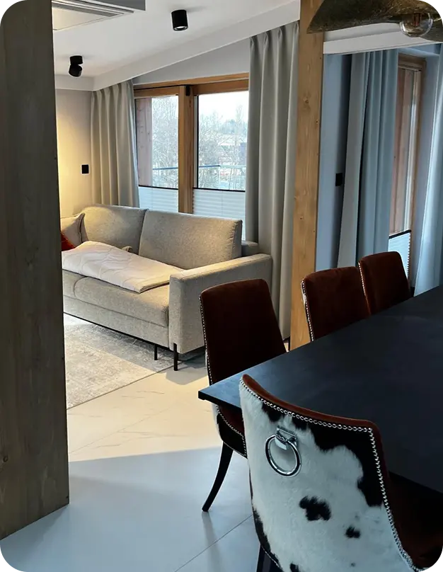 Przykład usługi Wykończenia wnętrz – salon z jadalnią: sofa, stół, krzesła i drewniane słupy