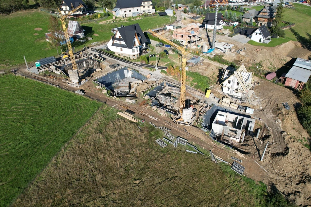 Widok z lotu ptaka placu budowy z wykopami, zbrojeniem i szalunkami fundamentów oraz żurawiami