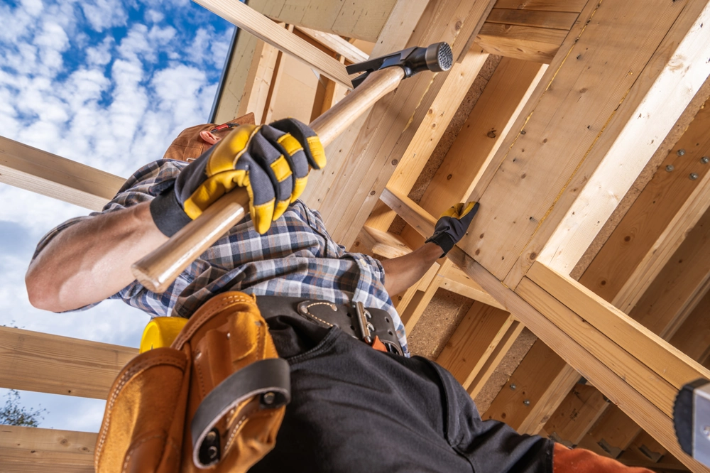 Mężczyzna montujący drewnianą więźbę dachową w konstrukcji budynku