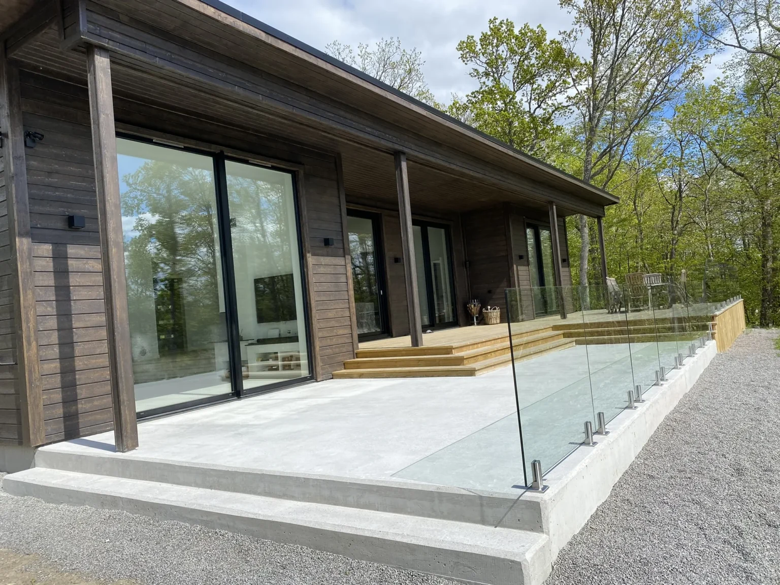 Dom z ciemną drewnianą elewacją, dużymi przeszkleniami i betonowym tarasem ze szklaną balustradą – nasza realizacja w Szwecji